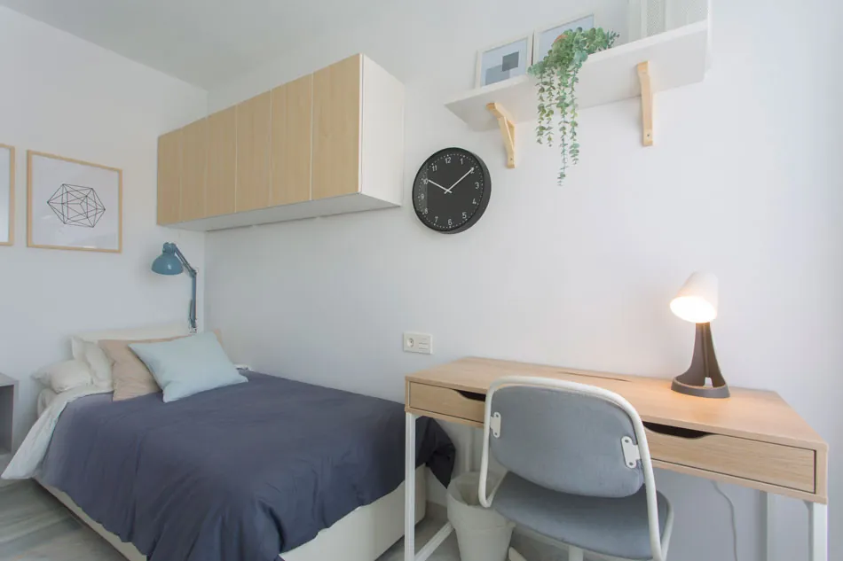Habitación de piso-residencia con cama, escritorio de madera clara y reloj de pared